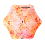 A hexagonal outdoor umbrella with a vibrant watercolor design in shades of orange, pink, and yellow, decorated with red hand-drawn sketches of marine life and sea plants. The brand name 'KAVU' is visible on a small black label at the bottom center.