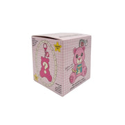 A pink gingham blind box featuring cartoon teddy bear illustrations and a large question mark on the front, photographed on a light gray studio background.