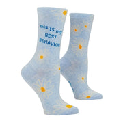 A pair of light blue crew socks with a daisy pattern and the text 'this IS my BEST BEHAVIOR' printed in blue on the side, displayed against a light gray background.