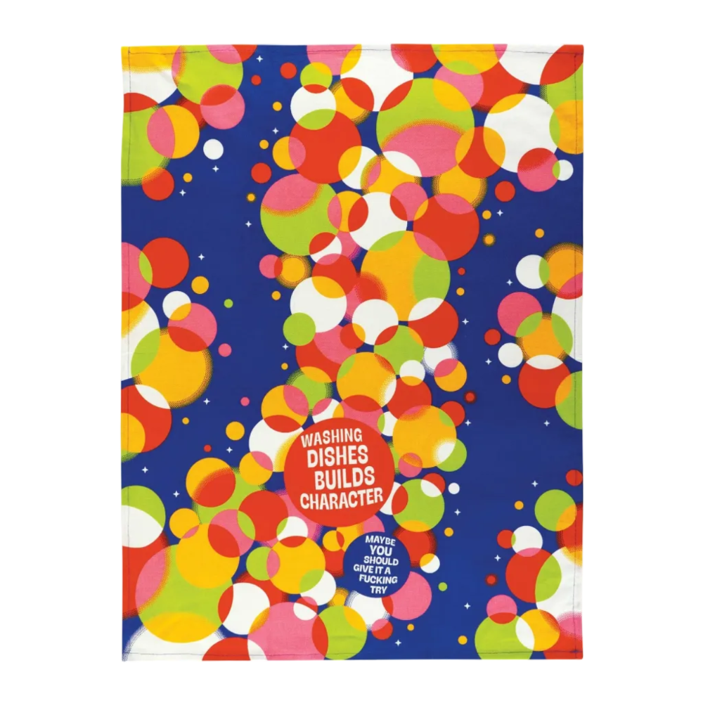 A square novelty towel featuring a retro pattern of overlapping colorful circles in red, orange, yellow, green, pink, and white on a dark blue background. The bottom center includes printed text reading 'WASHING DISHES BUILDS CHARACTER' and a small blue badge that says 'MADE IN USA WITH LOVE BY A FUCKING TOY'.