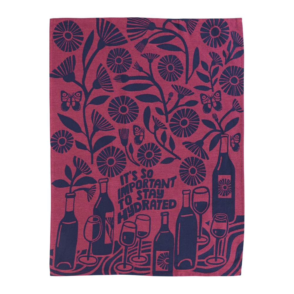 A rectangular tea towel with a dark navy blue botanical pattern and wine-themed illustrations on a dusty rose background. The design features flowers, butterflies, wine bottles, wine glasses, and the text 'IT'S SO IMPORTANT TO STAY HYDRATED'.