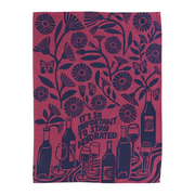 A rectangular tea towel with a dark navy blue botanical pattern and wine-themed illustrations on a dusty rose background. The design features flowers, butterflies, wine bottles, wine glasses, and the text 'IT'S SO IMPORTANT TO STAY HYDRATED'.