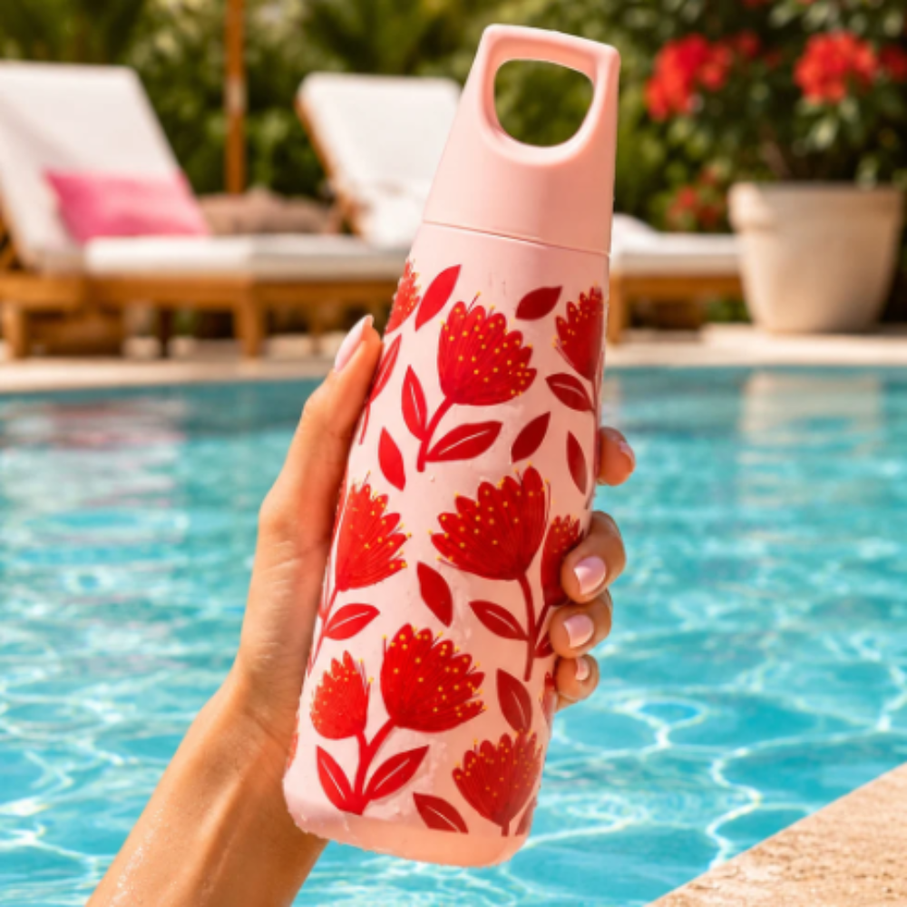 Person holding a pink water bottle with red floral pattern by a pool
