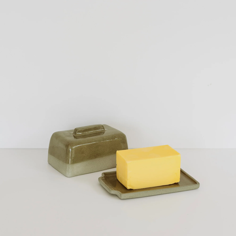 A ceramic butter dish set with a matching lid and tray, shown with a yellow block of butter on a neutral white background.
