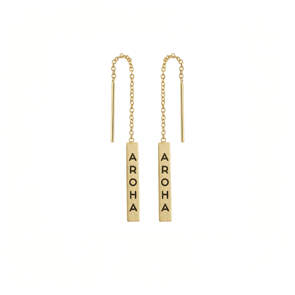 A pair of gold barbell drop earrings with short chains, each featuring a vertical rectangular bar engraved with the word 'AROMA' in black capital letters, shown on a plain white background.