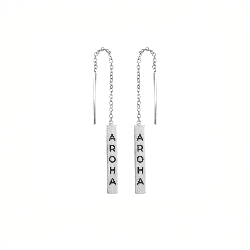 A pair of silver-toned dangle earrings with vertical rectangular bars engraved with the word 'AROMA' in black capital letters, suspended from delicate chains on a plain white background.