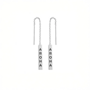 A pair of silver-toned dangle earrings with vertical rectangular bars engraved with the word 'AROMA' in black capital letters, suspended from delicate chains on a plain white background.