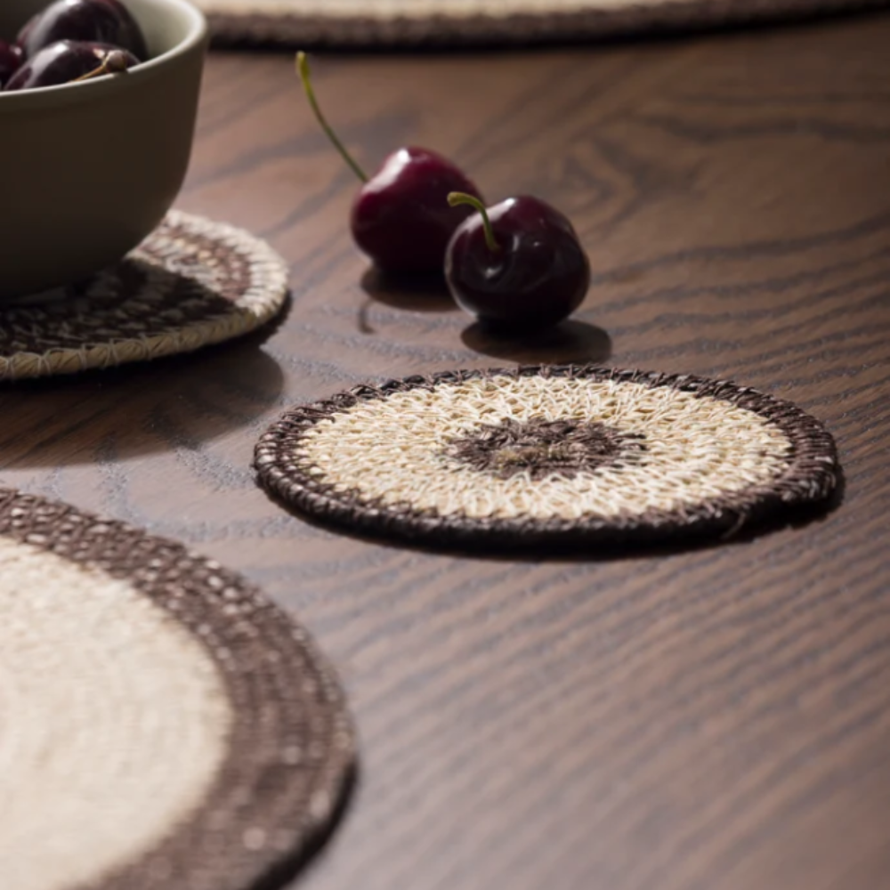 Woven coasters on a wooden table with cherries and a bowl.