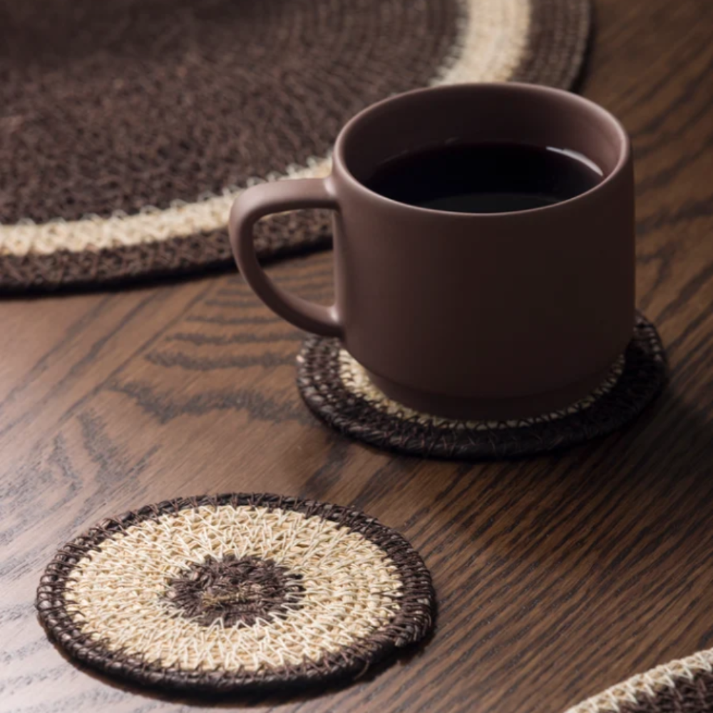 Brown mug on a woven coaster with matching placemats on a wooden table