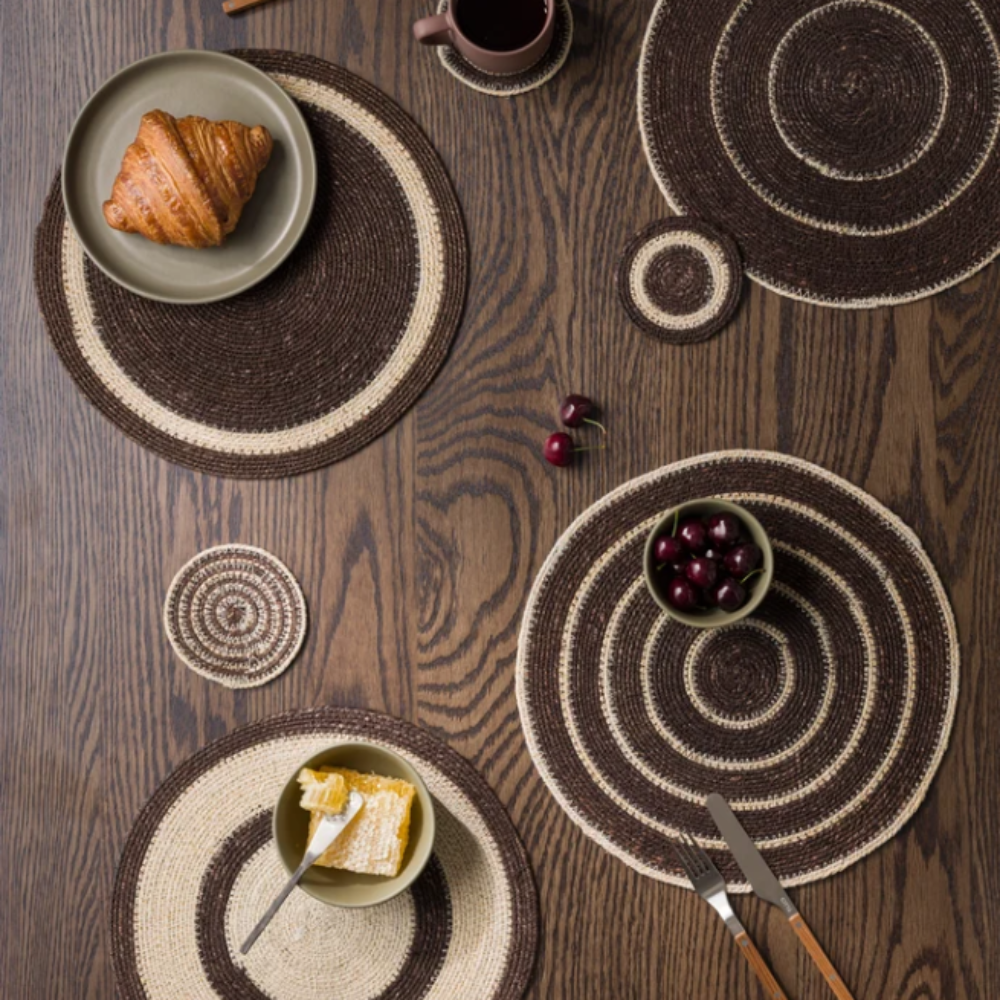 Woven placemats on a wooden table with food and cutlery