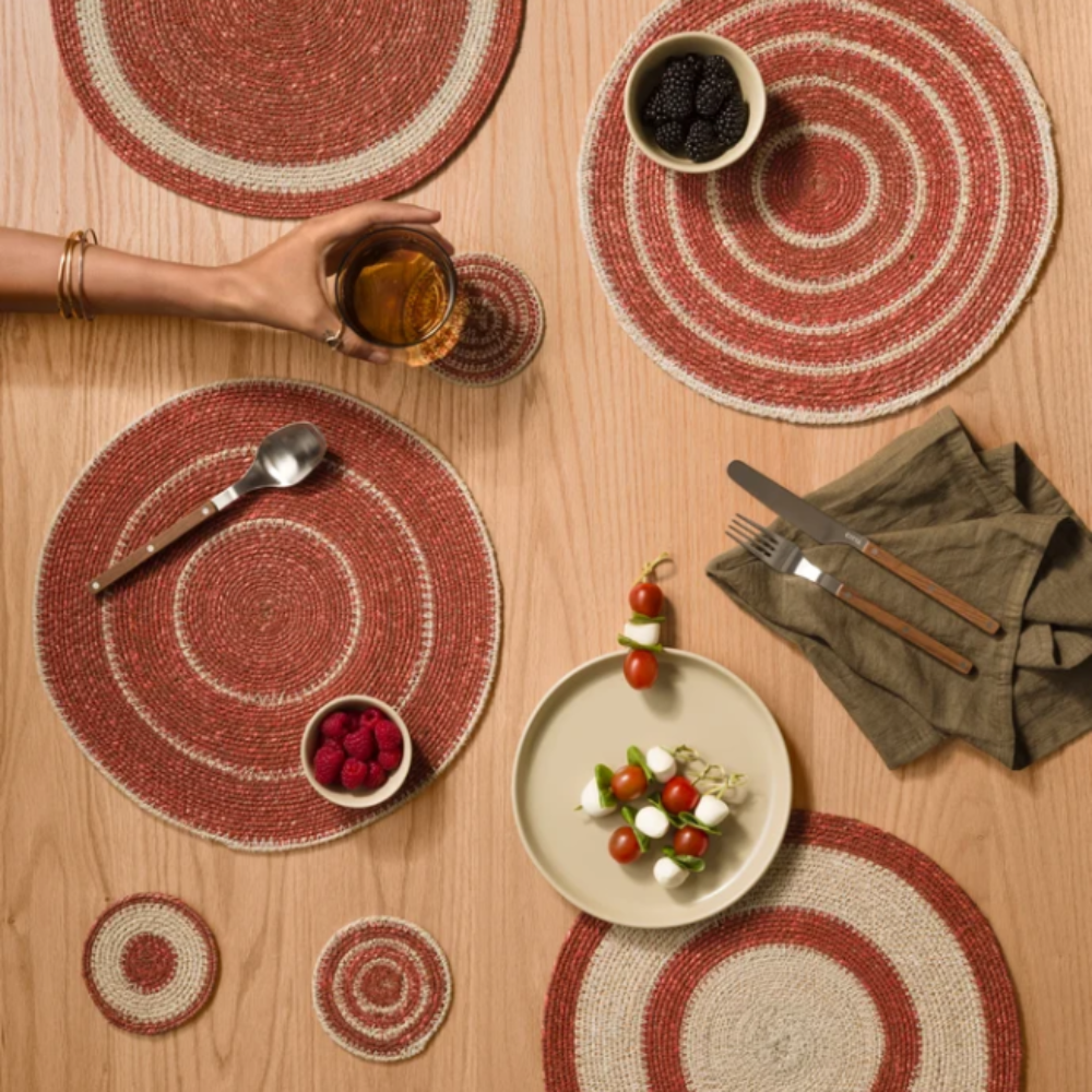Table setting with red and beige woven placemats on a wooden table.