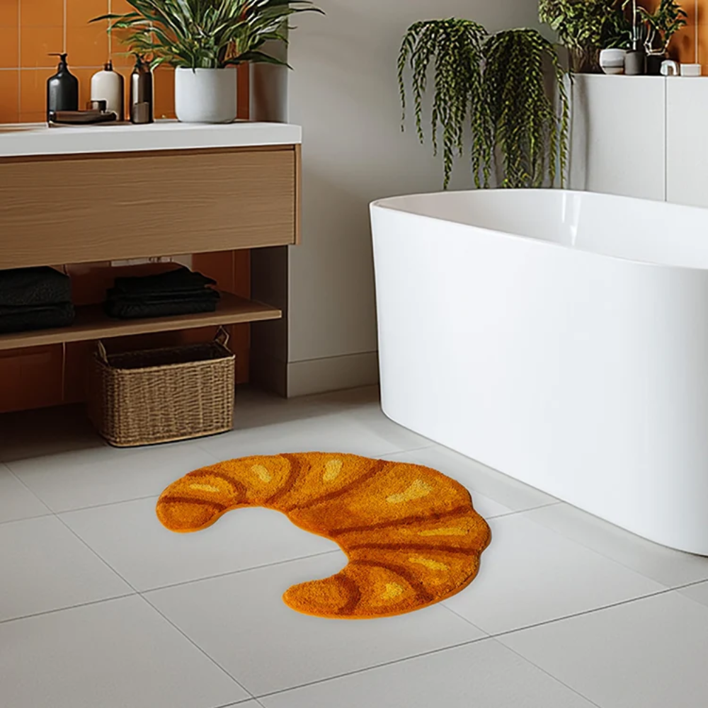 Orange bath mat shaped like a fish on a tiled bathroom floor with a white bathtub and wooden cabinet in the background.