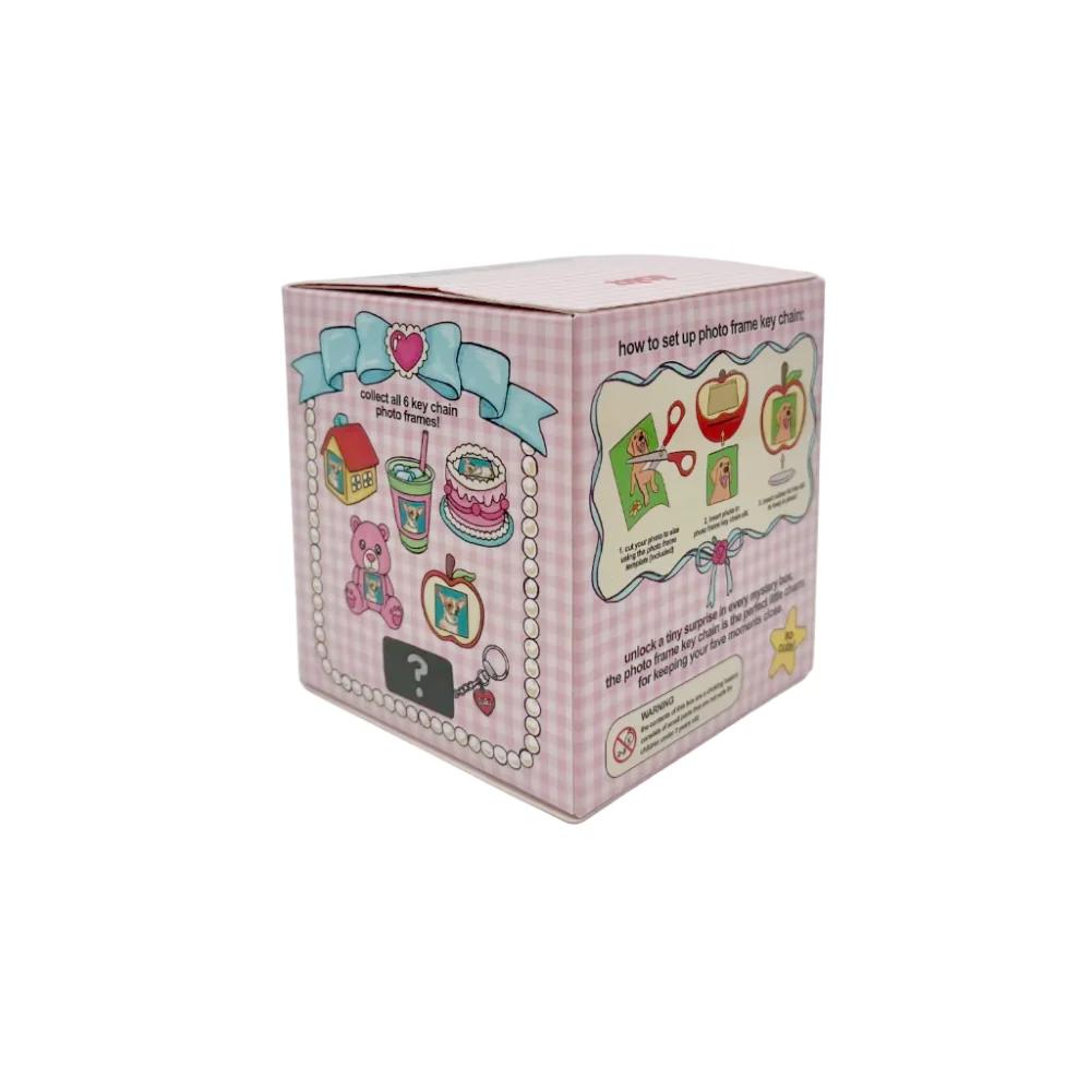 A pink and white checkered box with colorful illustrations of miniature toy items, photographed on a light gray studio background.