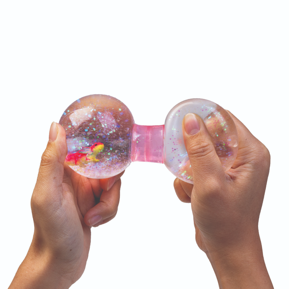 Two hands squeezing a pink bumpy stress ball toy with glitter and colorful internal elements, shown against a plain white background.