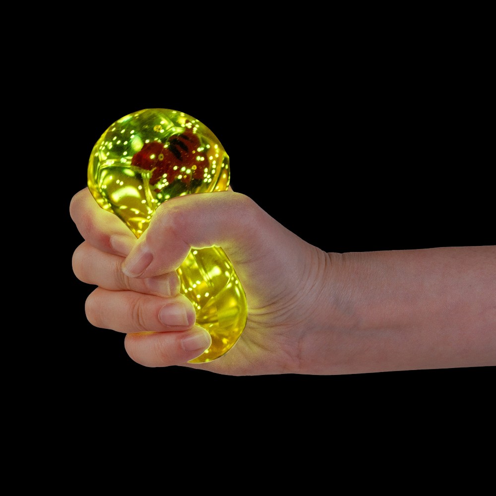 A hand squeezing a translucent yellow stress ball with a red center against a solid black background.