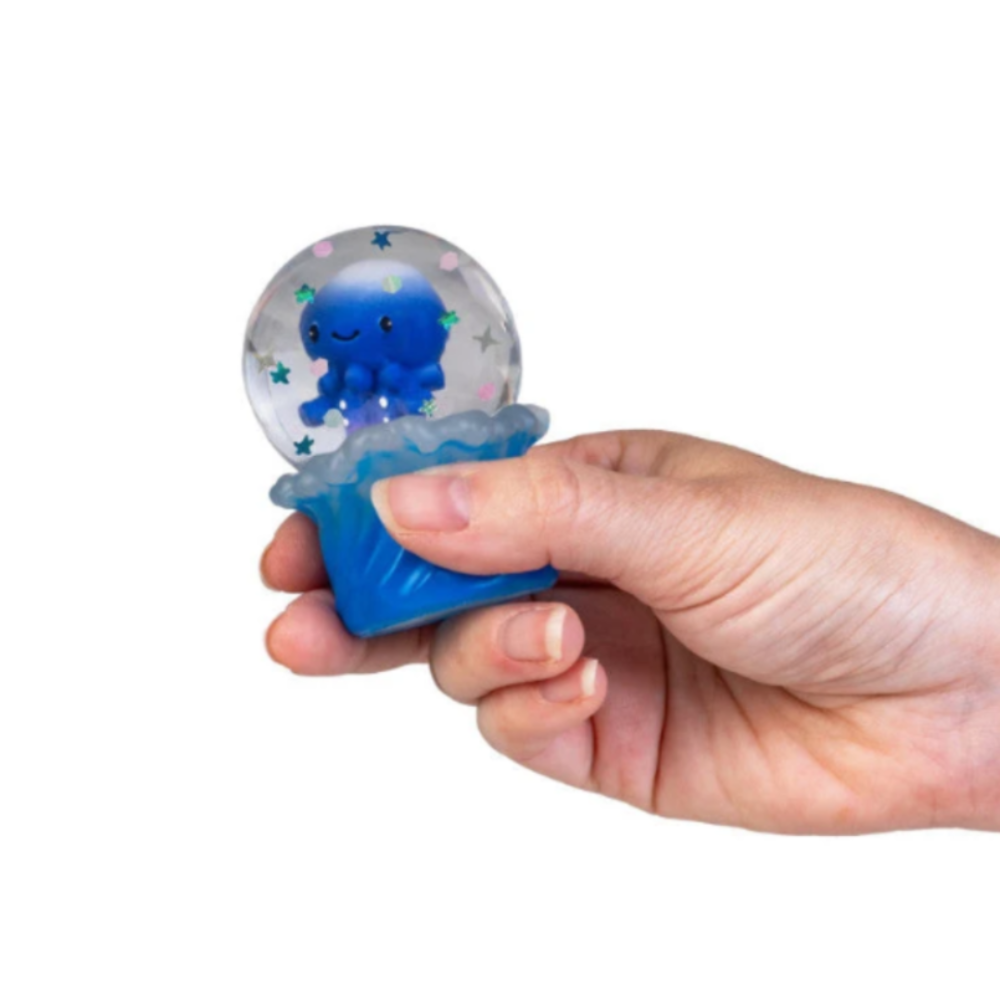 A hand holding a small blue octopus snow globe toy against a plain white background.