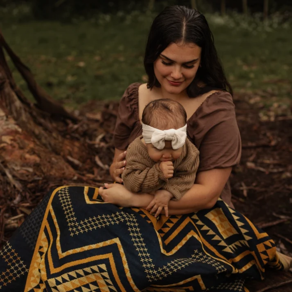 Woman holding a baby wrapped in a patterned blanket outdoors