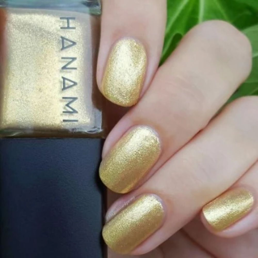Gold glitter nail polish with a hand displaying nails painted with the same color, next to a bottle of Hanami nail polish.