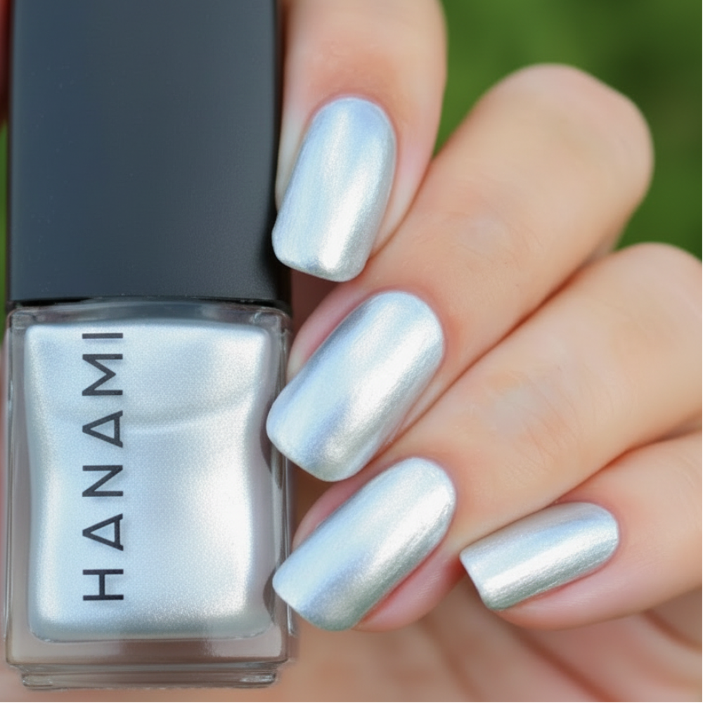 A close-up of a hand with fingernails painted in a metallic silver polish, standing next to a bottle of Hanami brand nail polish in the same shimmering silver shade.