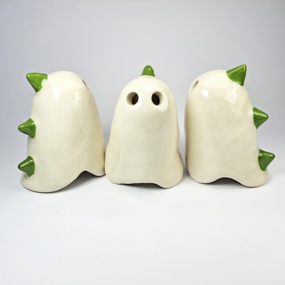 Three small ceramic ghost-shaped bird wind instruments in an off-white glaze with green spikes, shown on a light gray background.