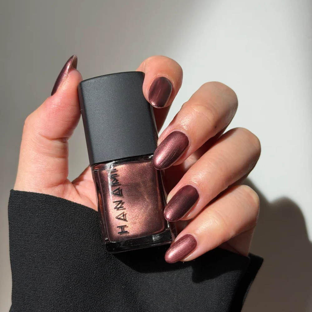Hand holding a bottle of HANAMI nail polish with matching nail color.