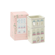 Paddywax Parisian Townhouse ceramic oil lamp and its pink packaging box, featuring a cream-colored house design with blue roofs and pink flower details.