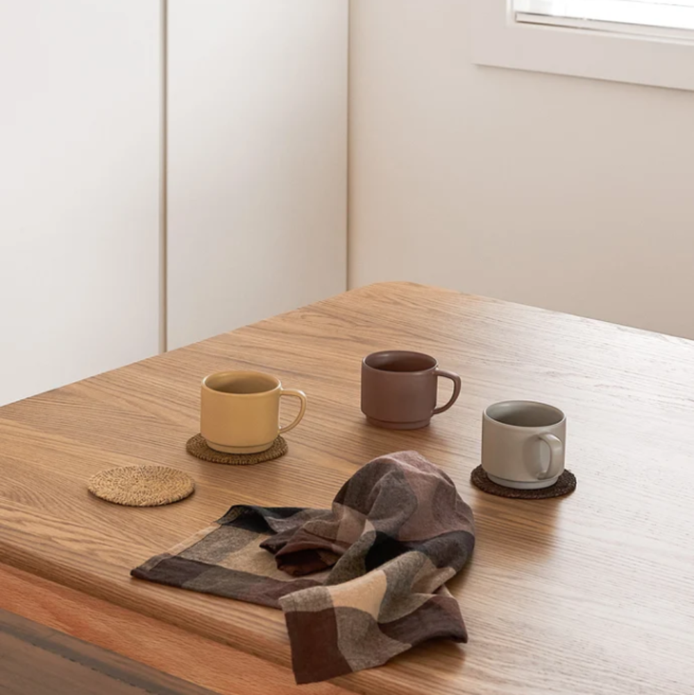 Three ceramic mugs on a wooden table with coasters