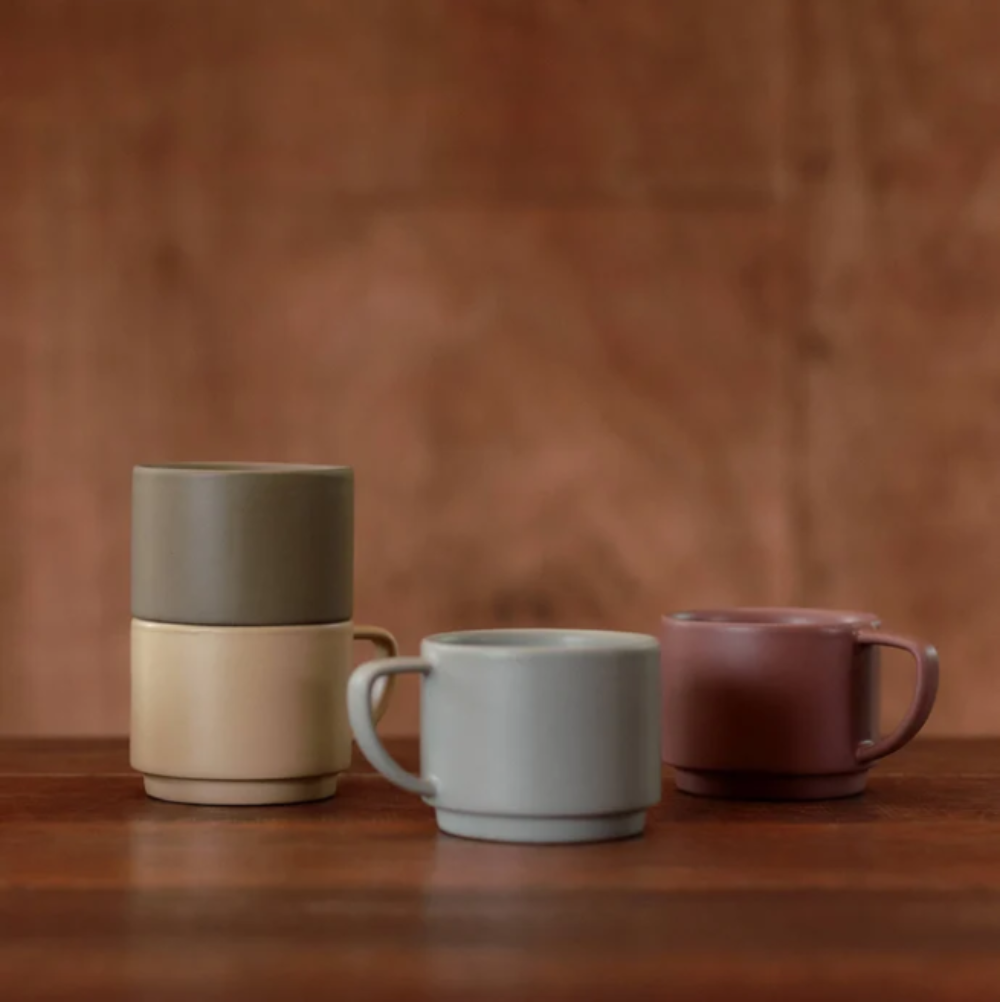 Four ceramic mugs in different colors on a wooden surface with a brown background