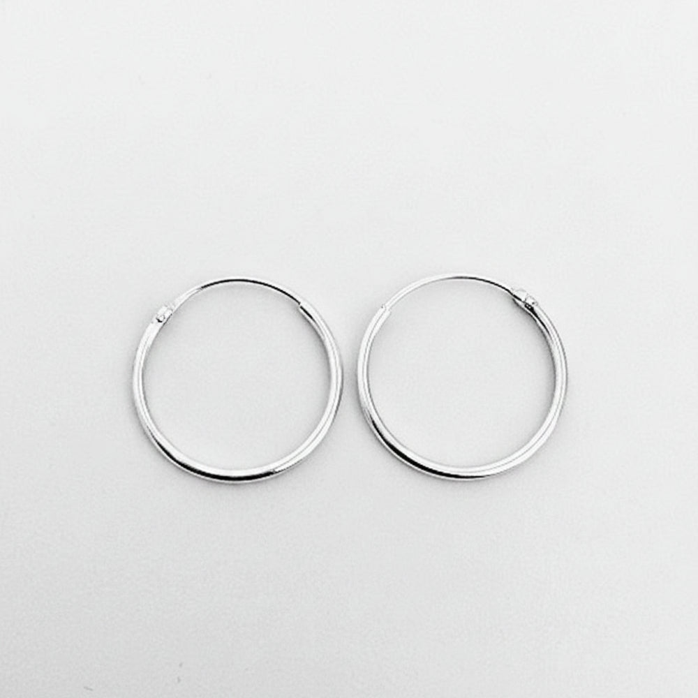 A pair of minimalist silver hoop earrings with a polished finish, displayed on a clean, light gray background.