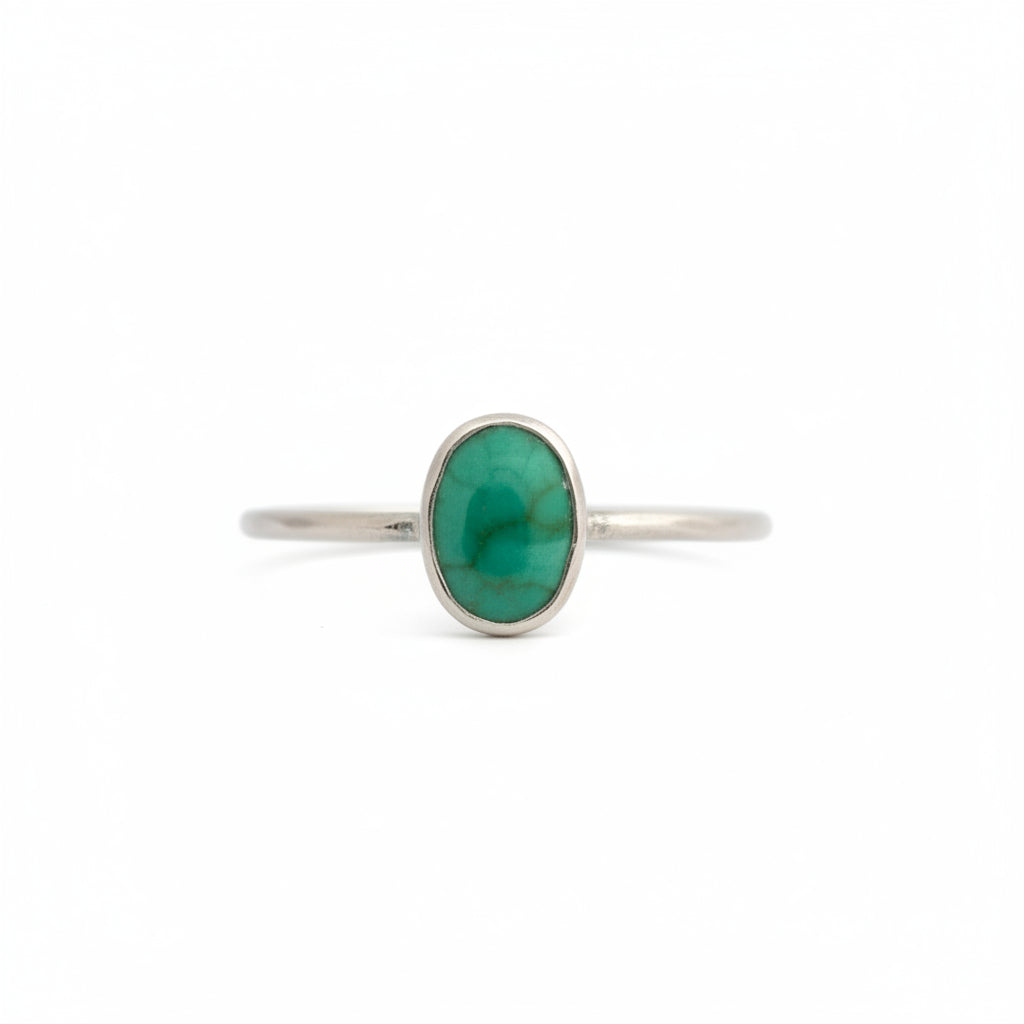 A delicate silver ring featuring an oval green stone, set against a plain white background.