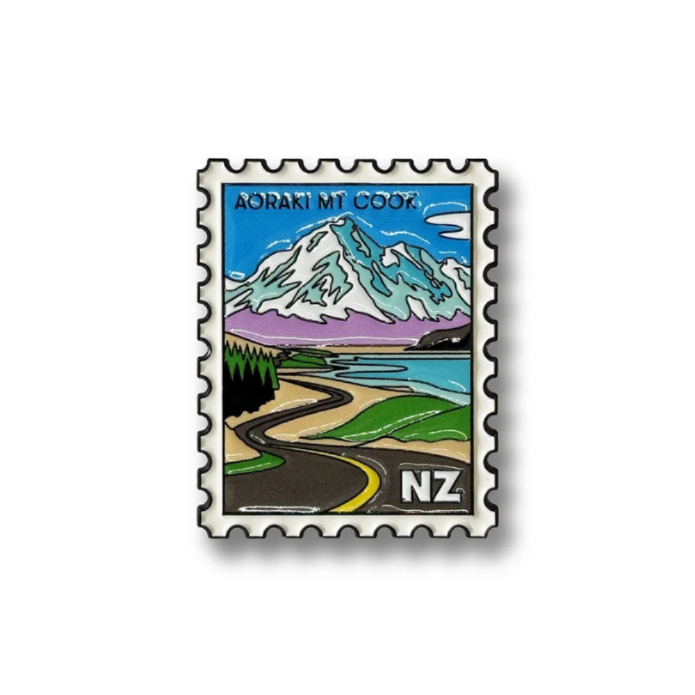 A rectangular postage stamp-style graphic with serrated edges featuring a stylized landscape of Aoraki Mt Cook, New Zealand. The illustration shows a snow-capped mountain, blue sky, lake, green hills, a winding road, and the text 'AORAKI MT COOK' at the top and 'NZ' at the bottom right.