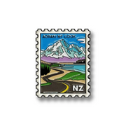 A rectangular postage stamp-style graphic with serrated edges featuring a stylized landscape of Aoraki Mt Cook, New Zealand. The illustration shows a snow-capped mountain, blue sky, lake, green hills, a winding road, and the text 'AORAKI MT COOK' at the top and 'NZ' at the bottom right.