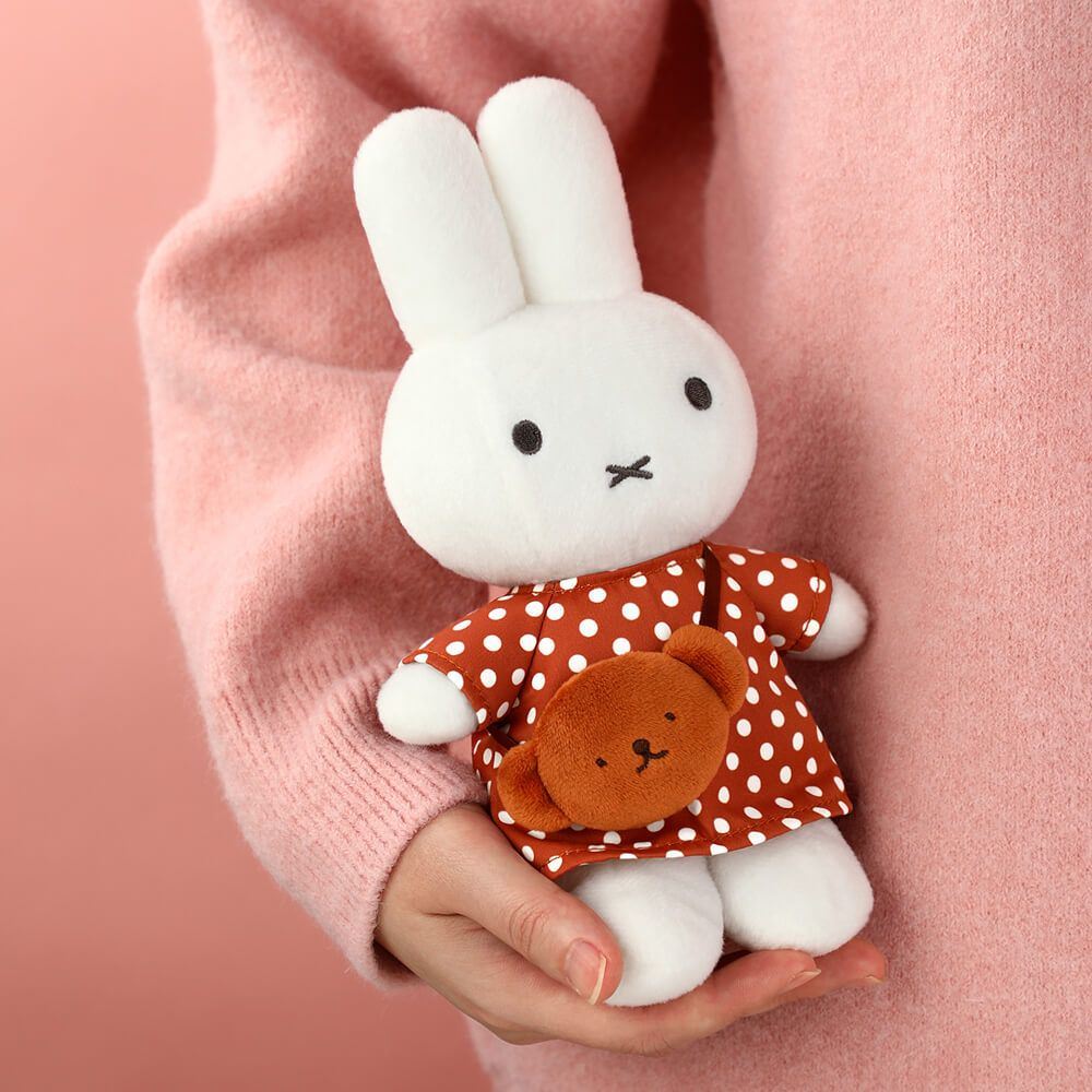 White plush bunny toy with a red polka dot dress held by a person wearing a pink sweater.