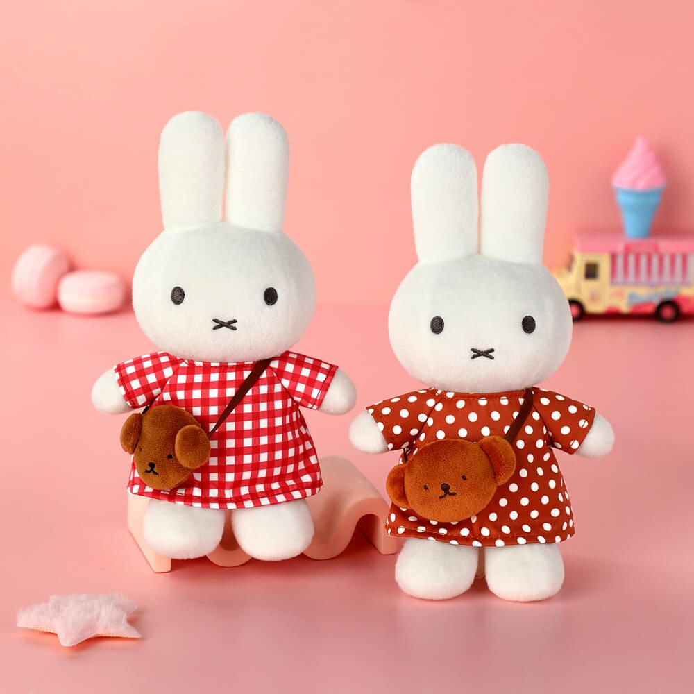 Two plush toys resembling bunnies in red outfits with brown bear accessories on a pink background.