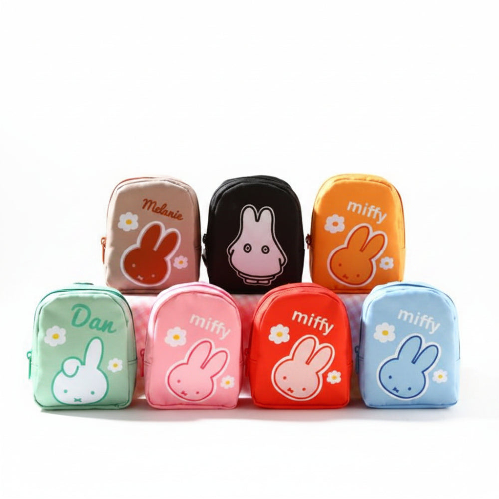 Six small zippered pouches or cases in different colors are arranged on a white surface against a bright yellow background. The cases feature cartoon rabbit illustrations and the words 'miffy' or 'Dan' printed on them.