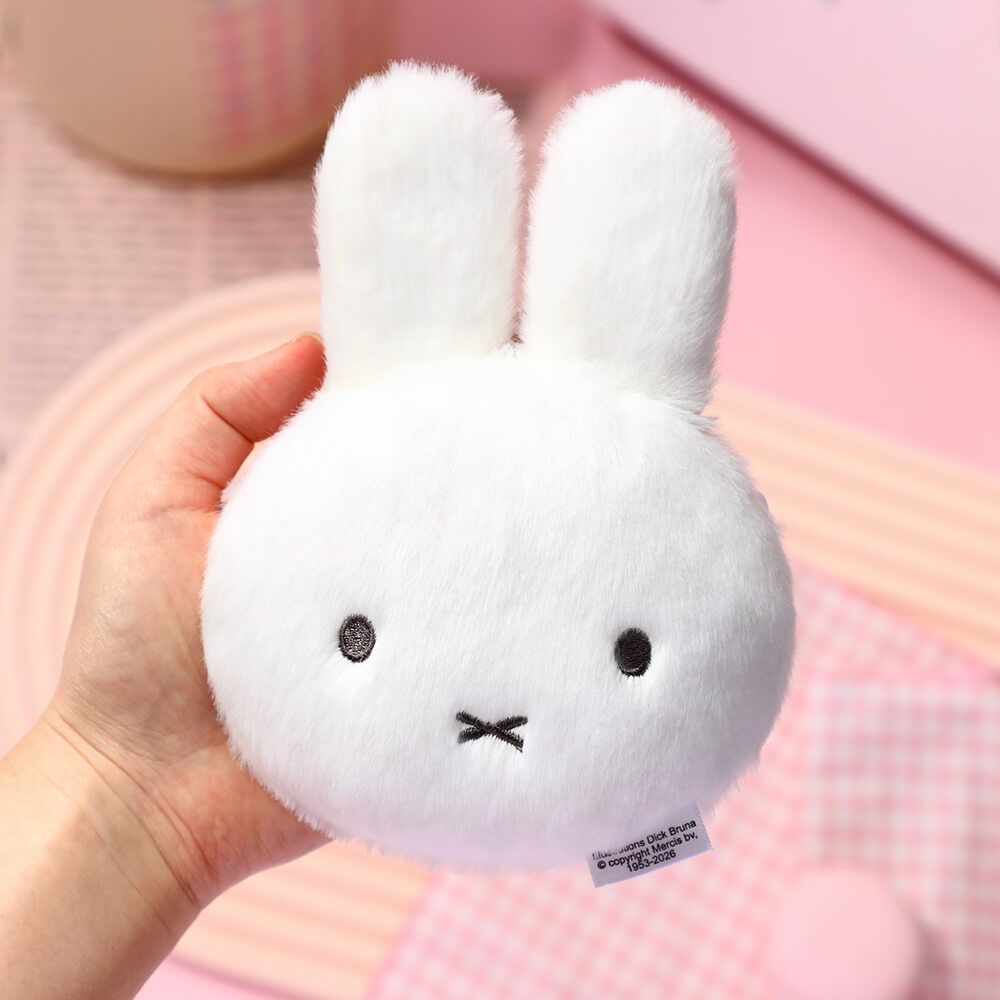 White plush bunny toy held in a hand with a pink background