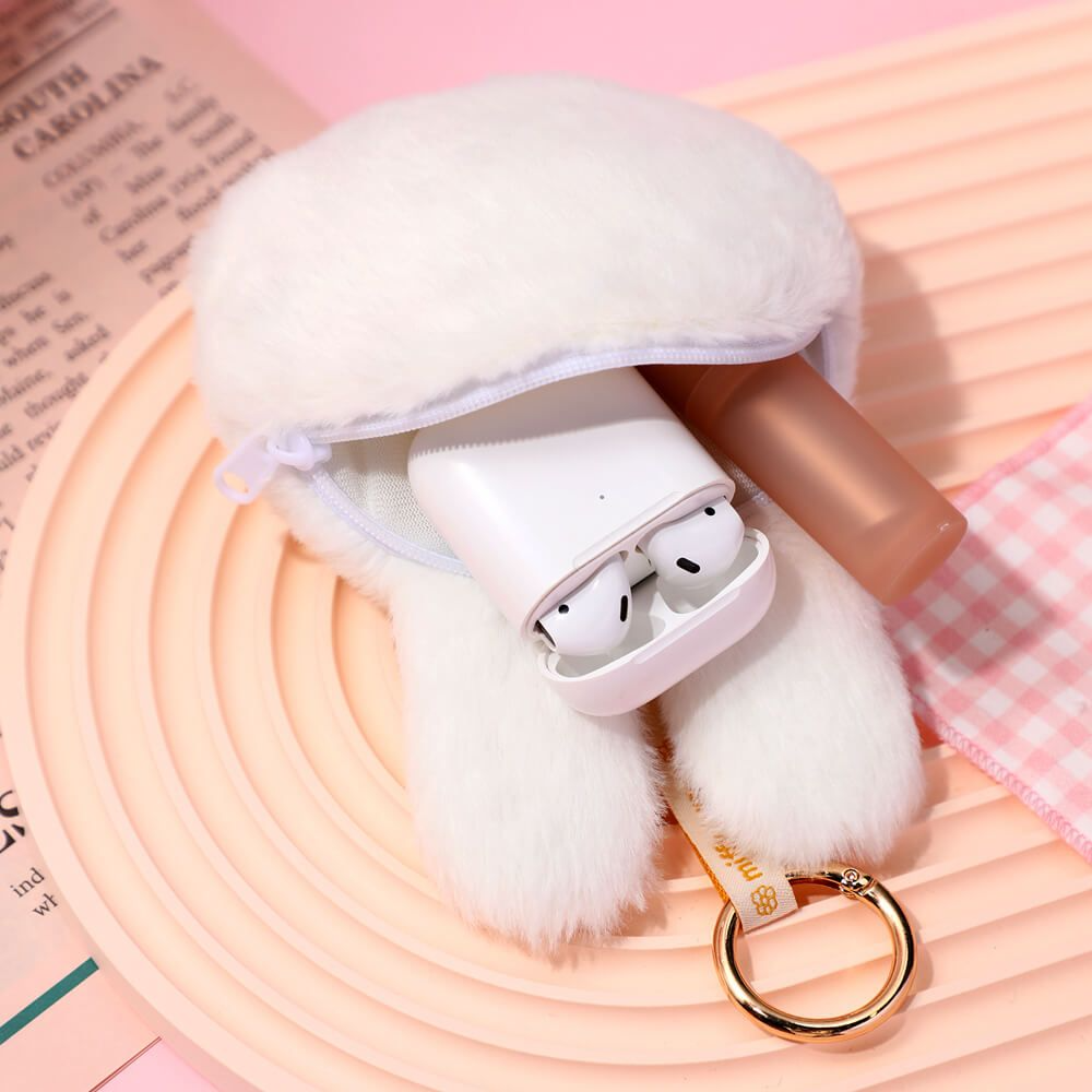 White wireless earbuds in a fluffy case with a gold keychain on a pink and white checkered background.