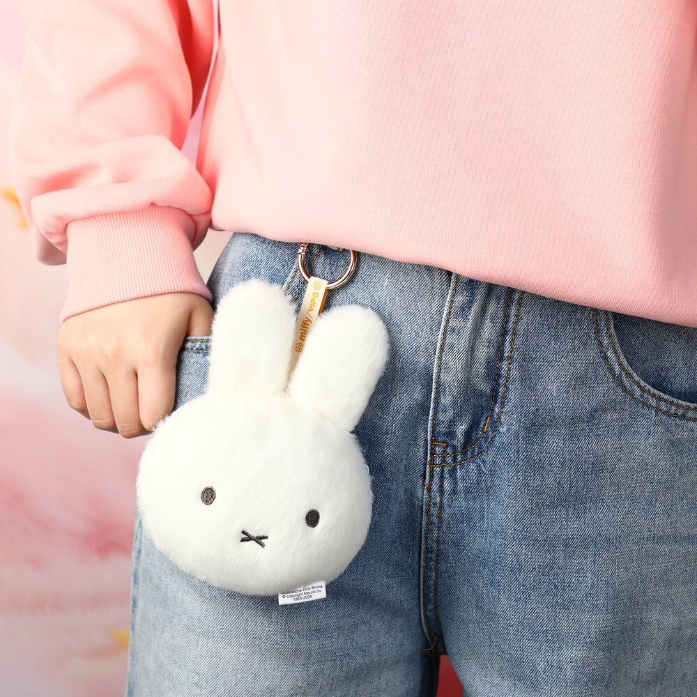 White plush bunny keychain held by a person wearing a pink sweater and blue jeans.