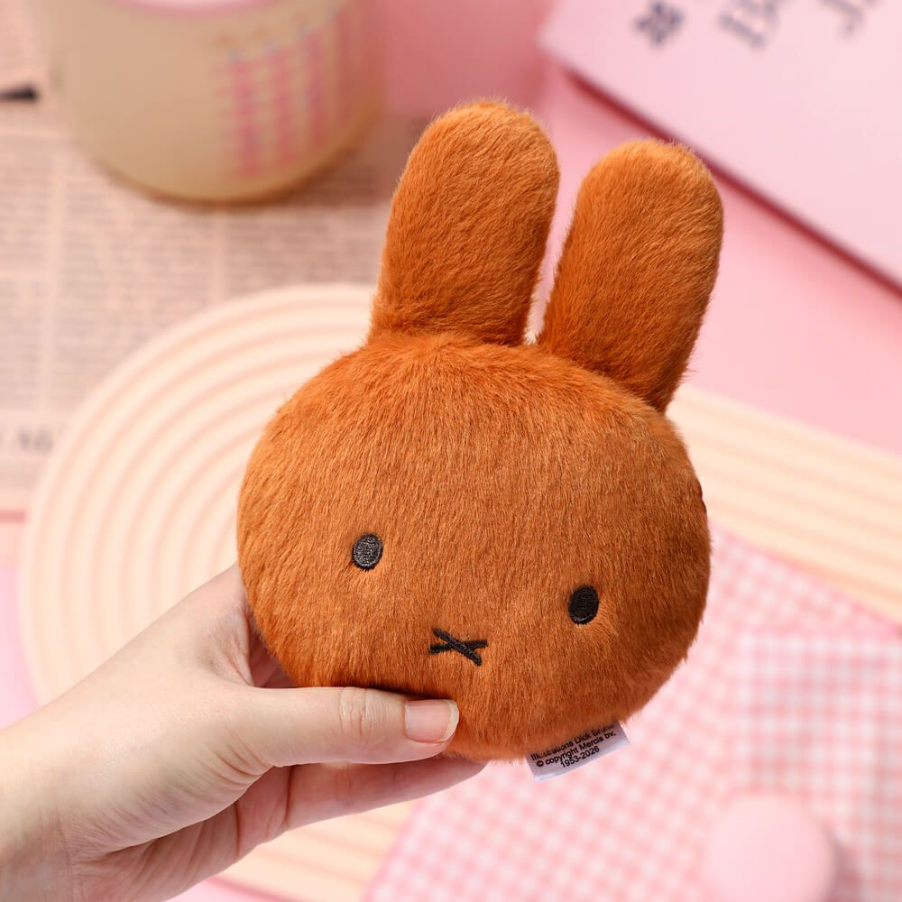 Small brown plush bunny held by a hand on a pink background
