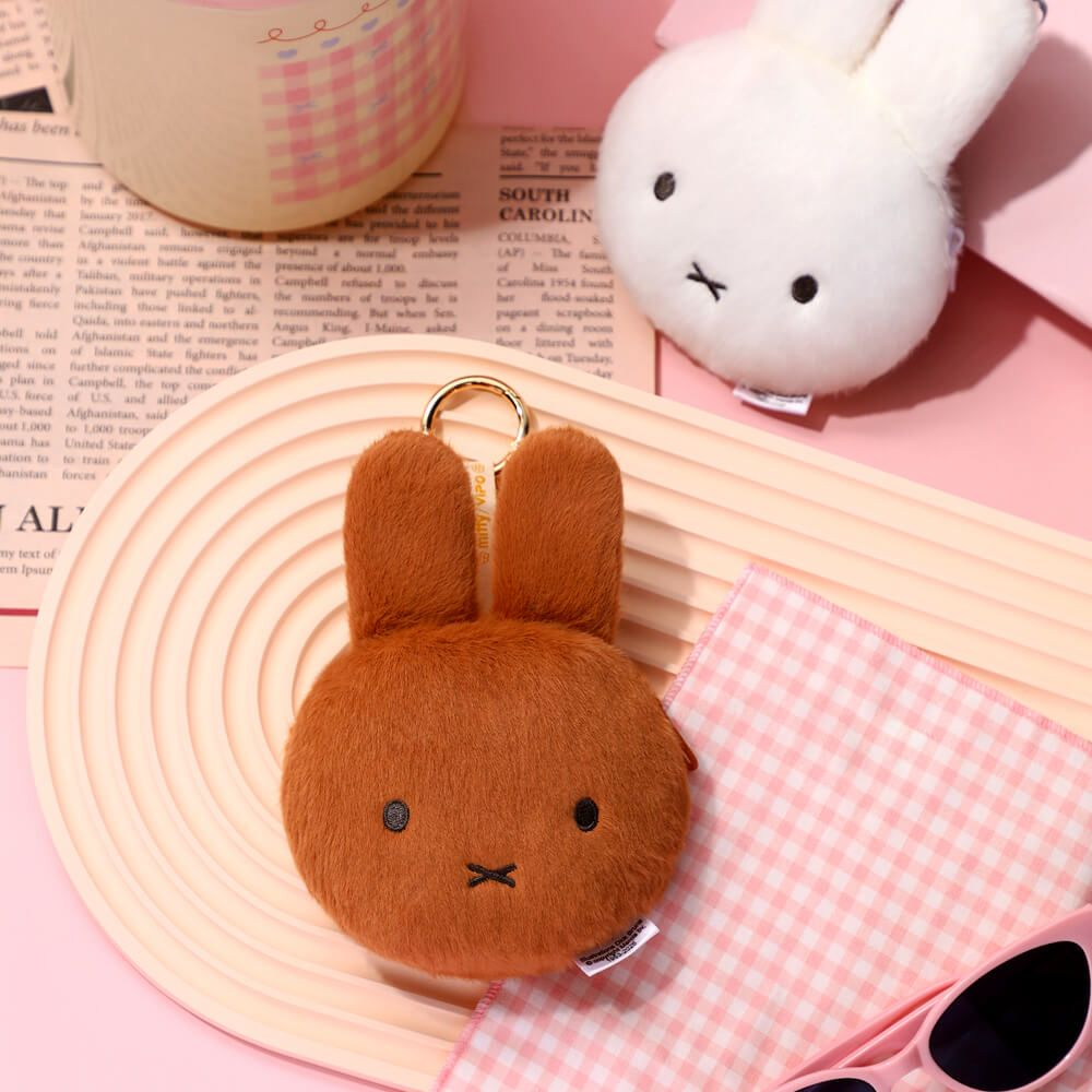 Brown plush bunny keychain on a pink surface with a white plush toy in the background.
