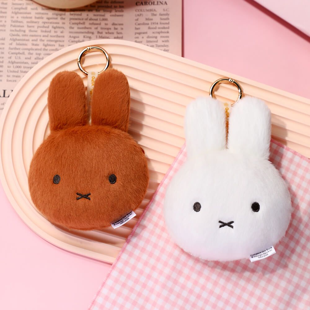 Two plush rabbit keychains, one brown and one white, on a pink checkered fabric background.