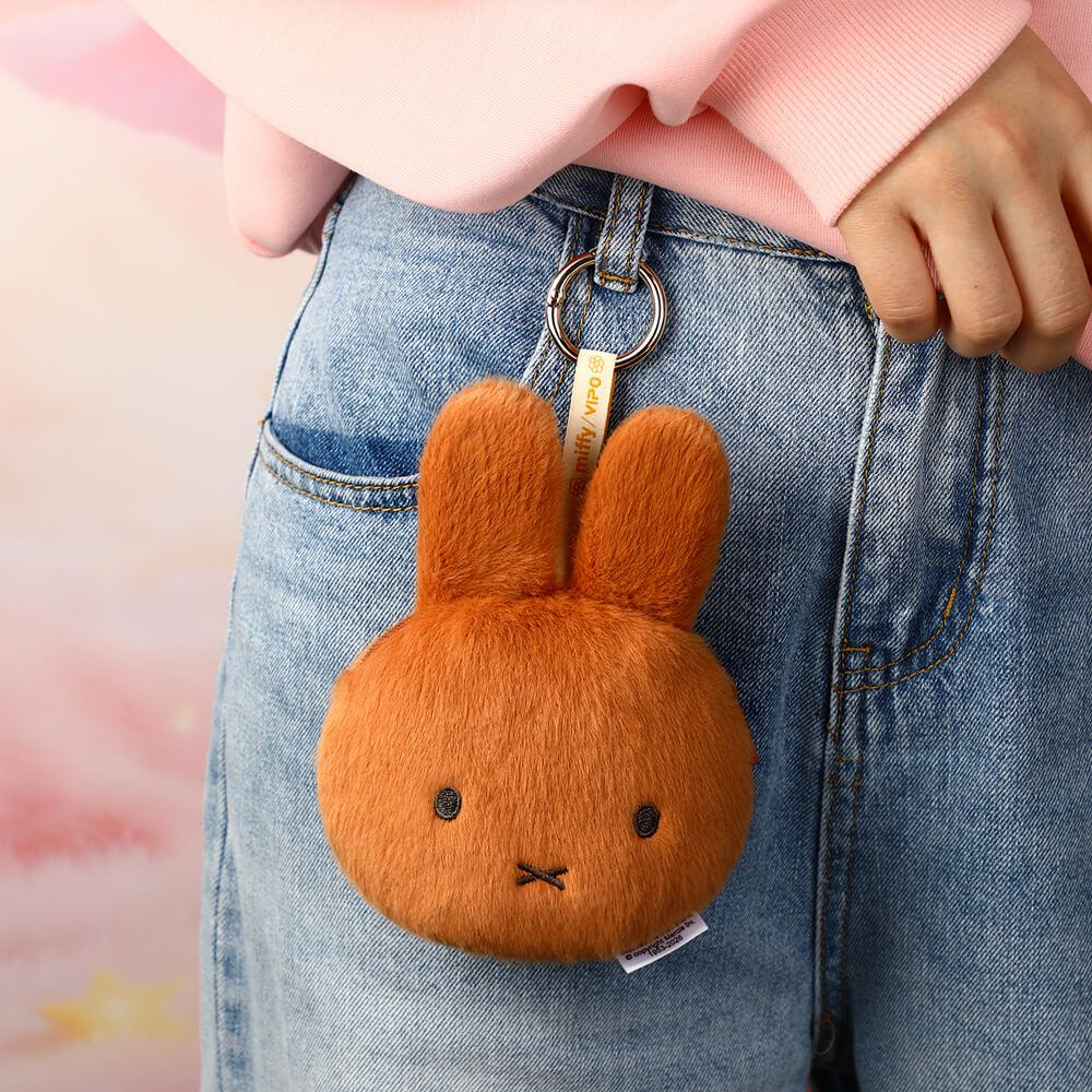A small orange plush bunny keychain or pouch hanging from a person's blue jeans pocket, with a pink top visible at the top of the frame.