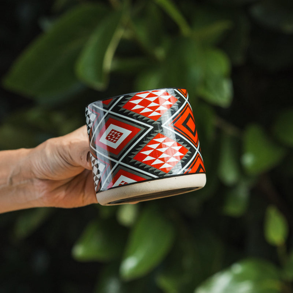 Person holding a mug with a colorful pattern against a green leafy background