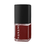 A bottle of Hanami nail polish in a deep burgundy red shade, featuring a black cap and clear glass base with the brand name printed vertically in white.