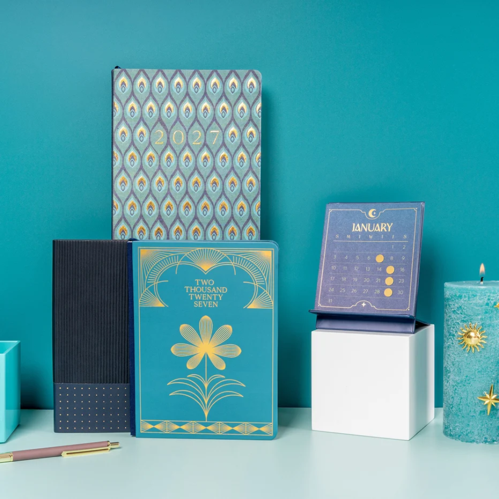 Collection of stationery items including a planner, calendar, and candle on a teal background