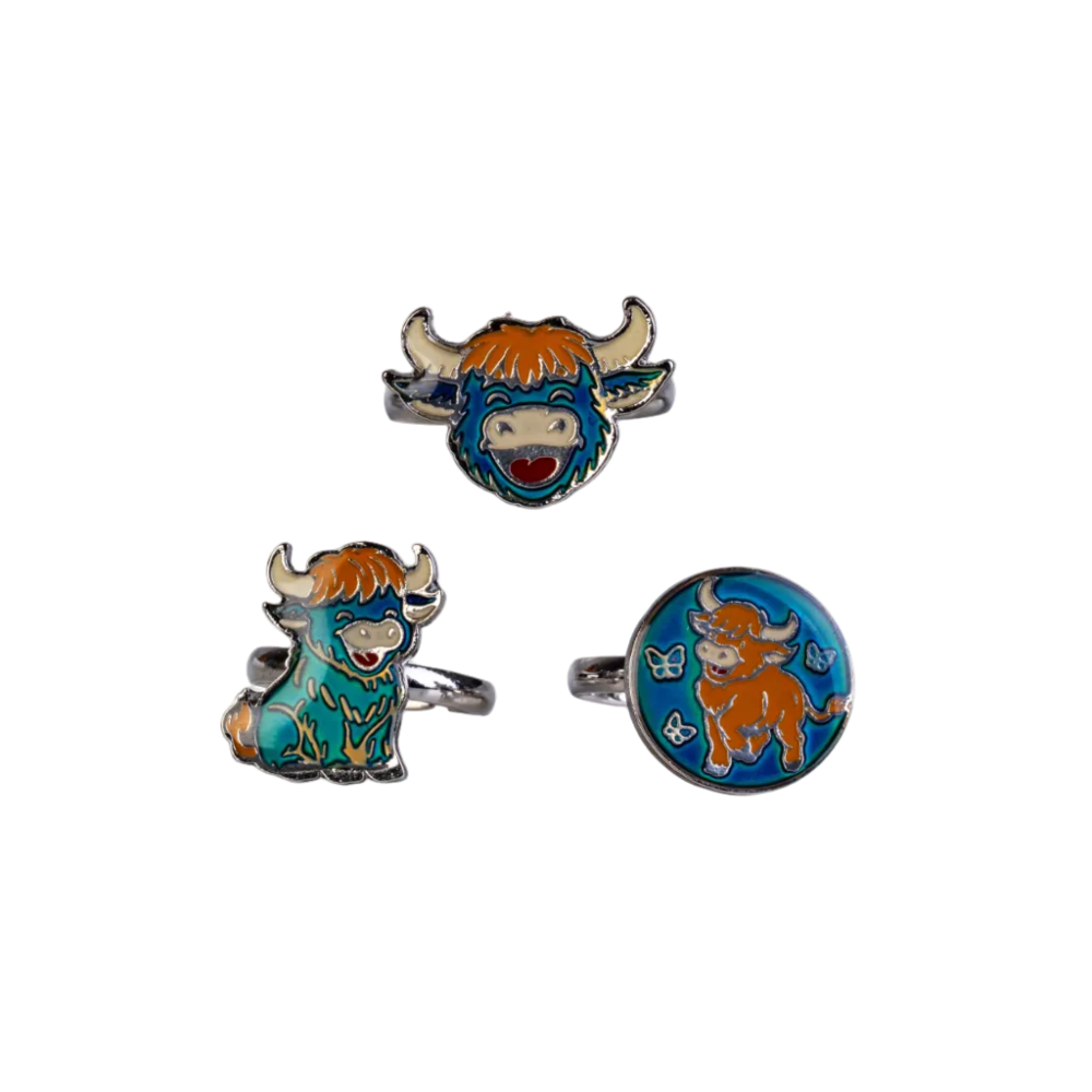 Three silver-tone bull-themed jewelry pieces on a plain white background: a bull head ring at the top, a seated bull charm at lower left, and a round bull face charm at lower right. The bull features orange hair, a blue face, and a teal body with white and red details.