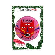A round pin-back button badge featuring a stylized red face with eyes, lightning bolts, and the words 'PUSSY POWER,' attached to a white display card with a green decorative border and text reading 'made with love' and 'magnet by Studio Soph'.