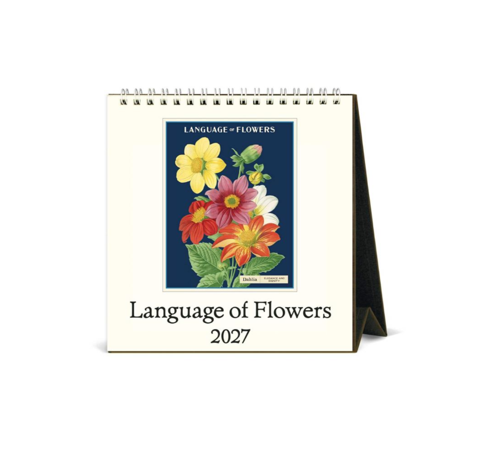 A spiral-bound 2027 desk calendar titled 'Language of Flowers' with a cream-colored cover, featuring a central botanical illustration of colorful flowers on a dark blue background and a black stand visible on the right.