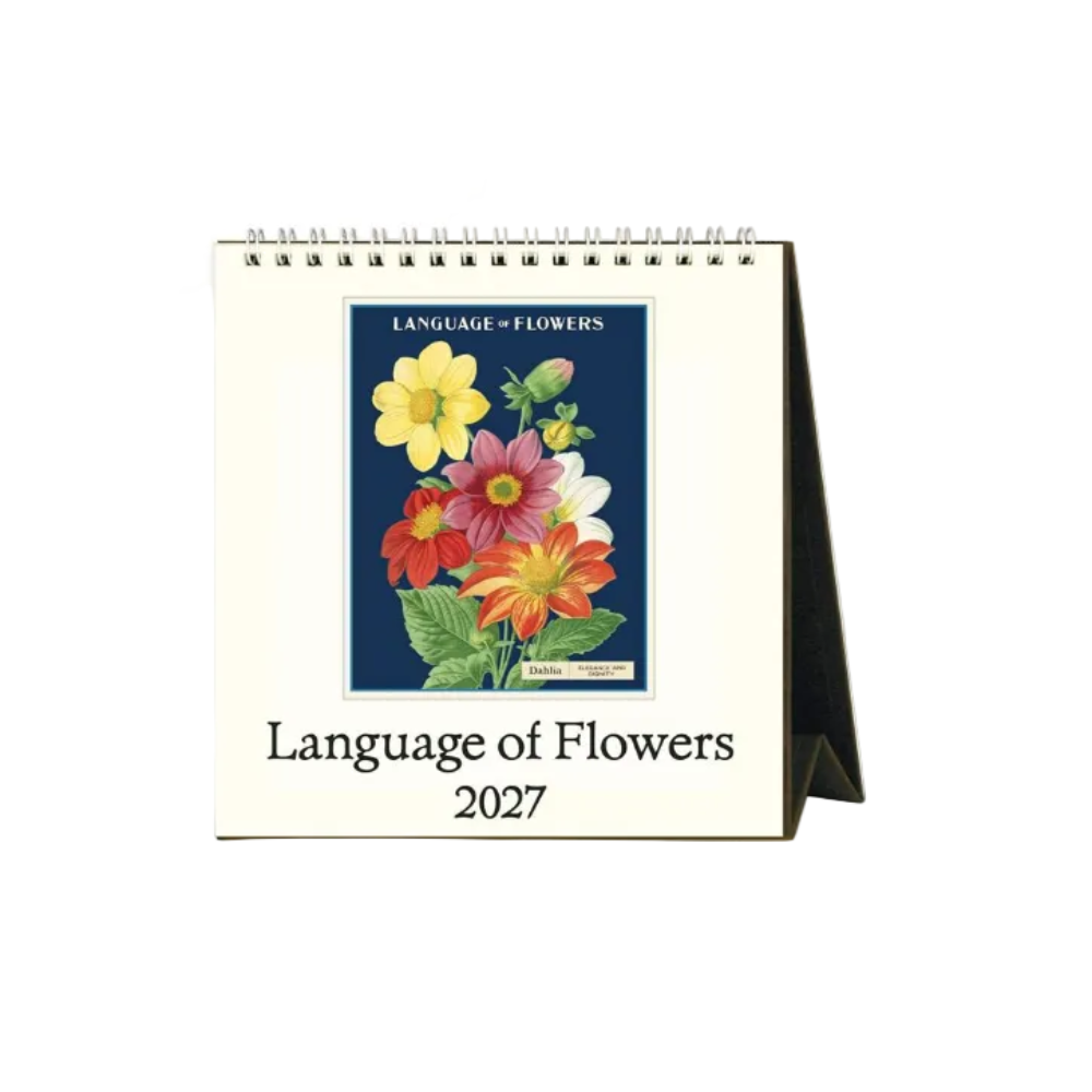 A spiral-bound 2027 desk calendar titled 'Language of Flowers' with a cream-colored cover, featuring a central botanical illustration of colorful flowers on a dark blue background and a black stand visible on the right.