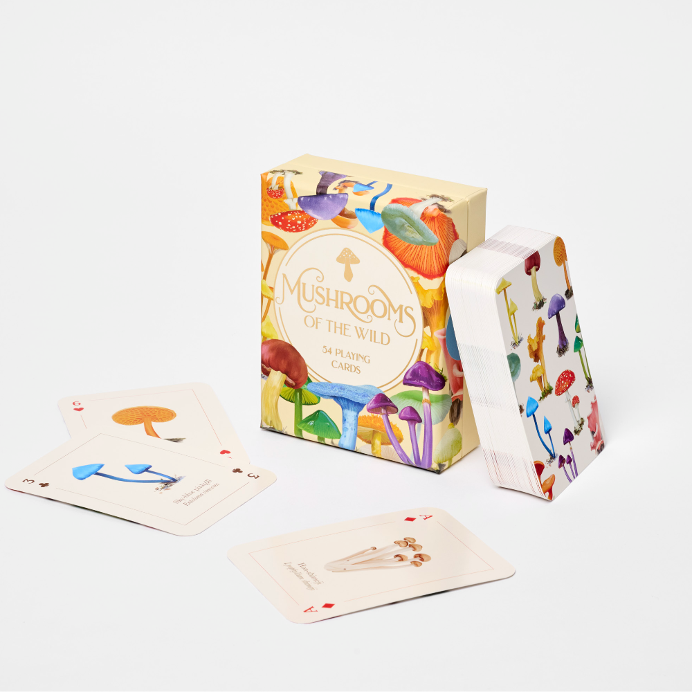A boxed card game called "Mushrooms of the Wild" with several illustrated cards fanned out around it on a clean white studio background. The box and card backs feature colorful mushroom artwork, and the cards are mostly off-white with small printed illustrations.